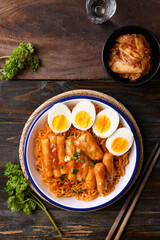 Korean spicy instant noodle with Tteokbokki, sausage and egg on wooden background, Table top view