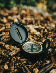 Black plastic opened compass on the forest floor surrounded by brown dead leaves at sunset