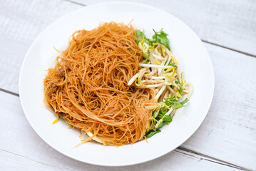 fried noodles vermicelli on white plate , Chinese styled fried noodle with bean sprout and coriander on wooden table - Thai food