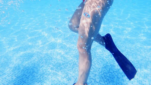 Cute girl with flippers in swimming pool at tropical beach, underwater view, slow motion