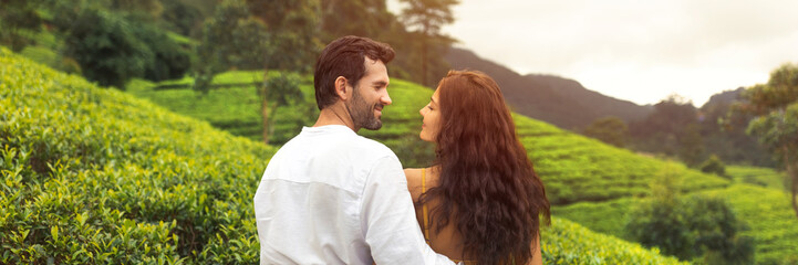 Romantic couple of travelers in love standing against nature background tea plantations landscape and looking to each other. Back view of young adult brunette woman and man in front of perfect natural