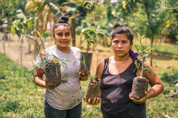 Nicaraguan women, mother and daughter holding plants in their hands and looking at camera in rural...