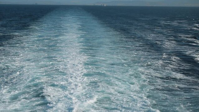 Waves from the back of a public ferry boat over the water's surface foam trace ship goes till the horizon as it travels across waving bright water