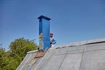 An employee of the Industrial Mountaineering Service paints the chimney on the roof with a spray...