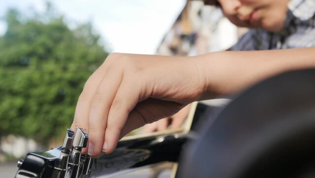 young guitarist boy spinning guitar pegs adjusting the sound and tension of an acoustic guitar while sitting in a park on a bench on a summer evening. Black guitar in the hands of a teenager