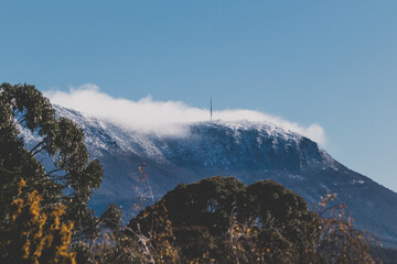 Snow on the mountain tops with clouds rolling over the pinnacles and thick Australian vegetation in the foreground shot in Tasmania,