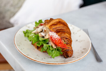 Delicious and healthy breakfast - croissant with chicken, tomatoes, lettuce and cream cheese on a plate.