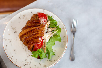 Delicious and healthy breakfast - croissant with chicken, tomatoes, lettuce and cream cheese on a plate.
