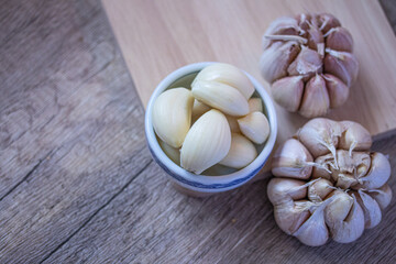 Peeled garlic in a bowl and garlic cloves on on a wooden chopping board