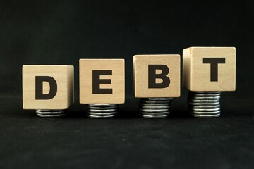 Increasing stack of coins with word debt in dark black background. Growing financial debts concept.	