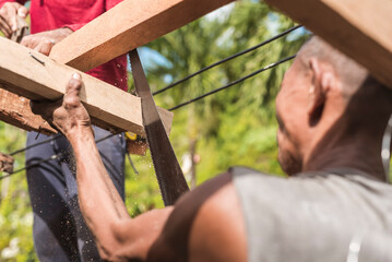 A carpenter saws off the excess edge of a wood rafter. Building or reconstructing a wooden roof frame for a rural home. - obrazy, fototapety, plakaty