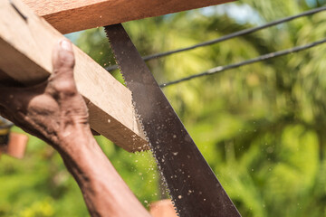 A carpenter saws off the excess edge of a wood rafter. Building or reconstructing a wooden roof frame for a rural home. - obrazy, fototapety, plakaty