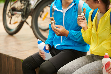 Cropped image of young couple eating granola bars to get some energy for bicycle ride