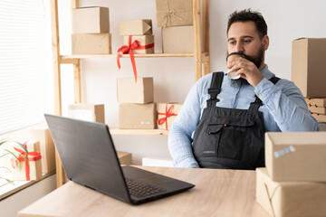 Small business aspiring indian entrepreneur drinking cofee, small and medium business freelance working in home office using computer, online marketing packaging box delivery, SME e-commerce