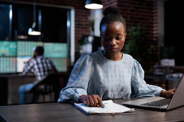 Finance company sales representant reviewing market trend documentation while sitting at desk in office at night. Forex stock agent analyzing financial charts while looking at paperwork clipboard.