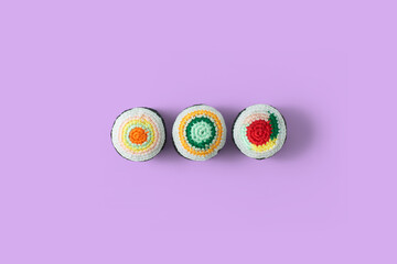 Delicious and fresh Set of traditional Japanese sushi rolls handmade in crochet and colored wool. Top view. Amigurumi sushi rolls isolated on a purple background
