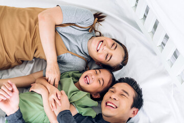 Obraz na płótnie Canvas Portrait enjoy happy smiling love asian family father and mother with young parents little child asian girl daughter play and looking together in moments good time lying on the bed at home