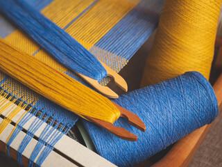 Hand loom with blue and yellow plain weave, two shuttles and yarn. Handwoven fabric creation in the process