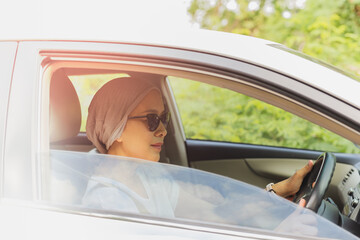 Asian woman wearing sunglasses driving a new car.