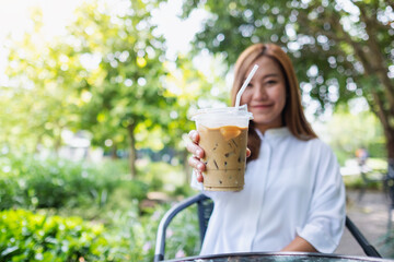 A young asian woman holding and giving a glass of iced coffee in the outdoors