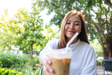 Portrait image a young asian woman holding and drinking iced coffee in the outdoors