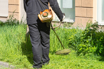a man mows the grass with a trimmer. improvement of the city