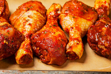 Asian style marinated chicken drumsticks on a brown baking paper and old baking tray ready to be cooked. Poultry product, summer range for barbeque. Red color marinate. Meat industry.