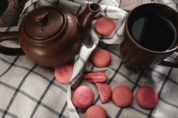 Obraz na płótnie Canvas Teapot and cup on kitchen cloth with scattered pink macarons