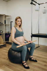 Pregnant woman exercising with the help of reformer on pilates class