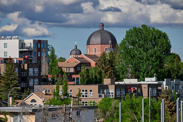 Obraz premium Incredible red brick temple with large metal dome with rust modern white buildings large round leafy trees apartments and offices sports courts blue skies with white clouds