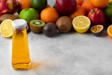 Various fruits and freshly squeezed fruits juice in bottle on gray background