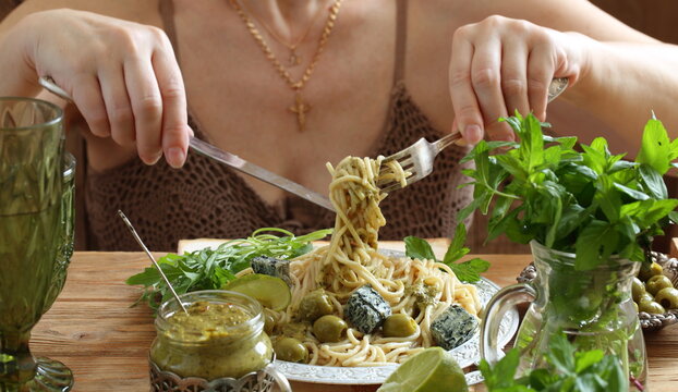 Female hands holding spaghetti with pesto sauce on a fork	
