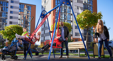 Happy family - father, mother and children having fun together on playground. Parents swinging...