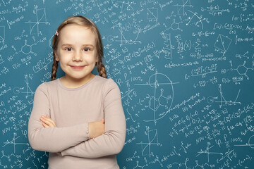 Successful female career concept. Cheerful little girl math student on blue school chalkboard background with hand drawings science formula pattern