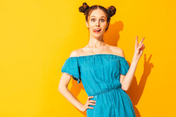 Young beautiful smiling female in trendy summer jeans overalls. Sexy carefree woman with two horns hairstyle posing near yellow wall in studio. Positive model having fun. Isolated