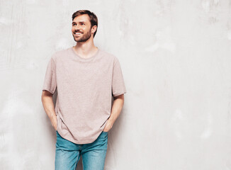 Portrait of handsome smiling stylish hipster lambersexual model. Sexy man dressed in pink T-shirt and jeans. Fashion male isolated on grey wall in studio