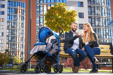 Happy family sitting with slipping in blue stroller baby. Smiling man tossing up keys from new...