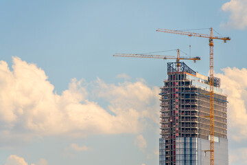 Construction cranes near the facade of a house under construction. modern building industry. Sale...