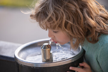 Face close up portrait of child drinking water from tap or water outdoor in park. Close up portrait...