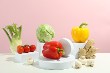 Vegetables on pedestals on white table against pink background