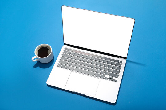 Open laptop with blank screen and cup of coffee on blue background