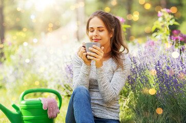 gardening and people concept - young woman drinking tea or coffee at summer garden