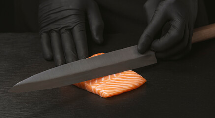 Close up of chef slicing salmon with sharp knife on black desk