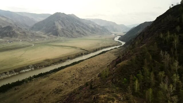 A river running along high mountains. Mountainous terrain. A small village. Aerial photography of spring nature.