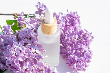 Serum or Liquid Collagen essence in frosted glass bottle on white background with purple lilac flowers. Anti age Cosmetics products concept.