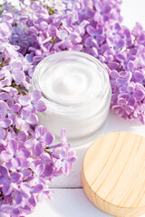 White jar of moisturizing face cream with bamboo cap on white wooden background with lilac flowers. eco cosmetology or skin care concept.