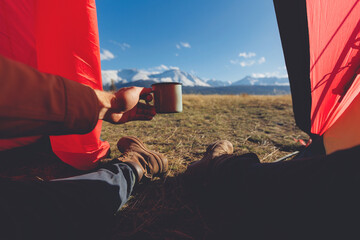 Traveler man with cup lying in red tent background view of mountains Altai