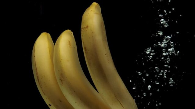 Slow motion bananas falling into transparent water on black background. Fresh fruits splashing in aquarium. Healthy food, diet, air bubbles