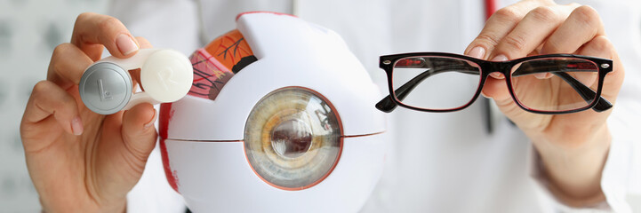 Ophthalmologist doctor holding eyeglasses and lenses near artificial model of eye closeup