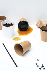 Disposable coffee cups, roasted coffee beans and spilling coffee on white table. Creative still life, copy space.